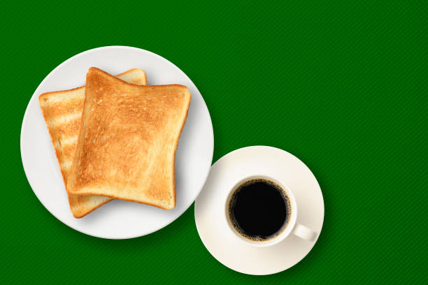 Overhead shot of two toasted bread on a white plate with a cup of coffee, on a green tablecloth.