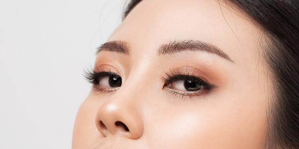 A close-up of a young Caucasian woman looking at the camera and applying mascara with a smile on her face.