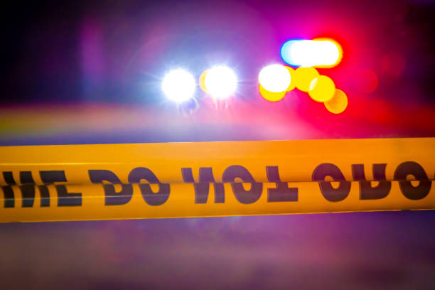 Generic police lights and yellow police tape at crime scene Generic and blurry police lights from a cruiser vehicle and car headlights behind yellow crime scene do not cross caution tape at night. cordon tape stock pictures, royalty-free photos & images