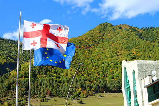 Georgian flag with EU Flag Waving Against the Early Autumn Hills of Mestia Town, Svaneti Region, Georgia