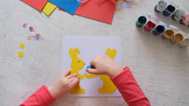 Child making card with Easter bunnies  from colorful paper. Applique. Handmade. Project of children's creativity, handicrafts, crafts for kids.