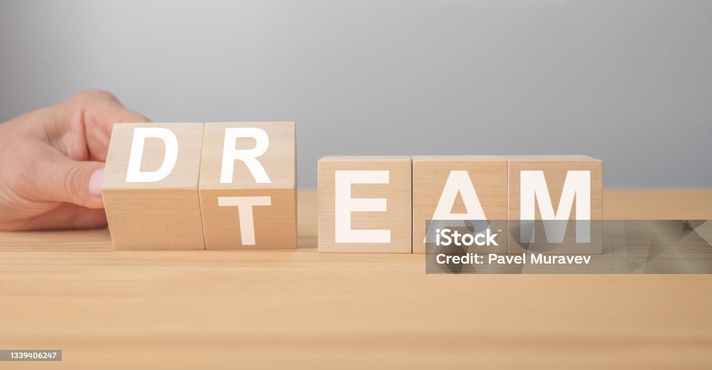 Dream team. Businessman turns cubes and changes the word dream to team. Wooden table, grey background. Business and dream team concept, copy space. Dream team on wooden cubes. Hand is turning a dice and changes the word dream to team. Dream Team message. Business and dream team concept, copy space Teamwork Stock Photo
