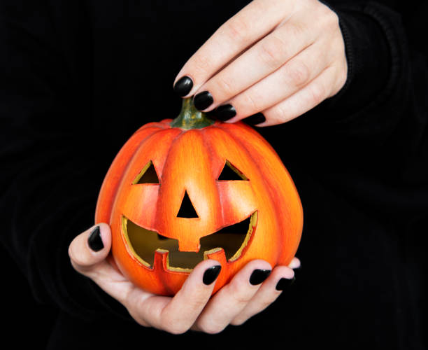 istock Female hands holding funny pumpkins on black background 1339410662