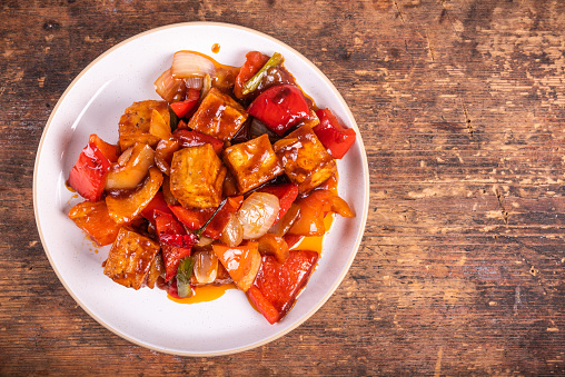 Tofu with onions and peppers fried stir-fry in spicy pepper sauce on a plate, top view, copy space for recipe