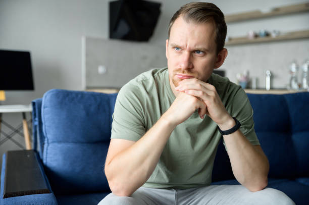 istock Worried guy sits on the sofa alone and looks away lost in thoughts 1339412334
