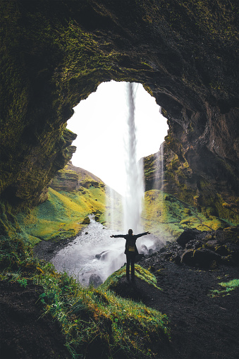 Woman with arms outstretched standing behind the waterfall in south of Iceland.