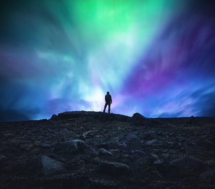 Man standing in the middle of an Icelandic wilderness and watching aurora borealis.