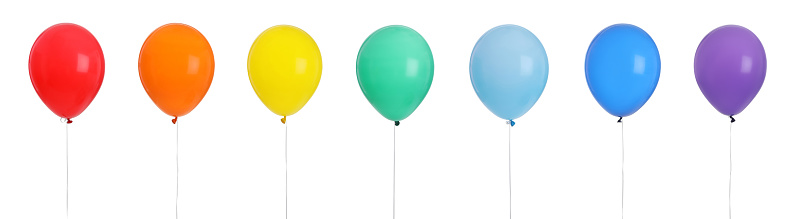 A large collection of colorful balls or balloons flys through the streets of a city. They fly towards the sky and pass by large buildings. It is a surreal sight.