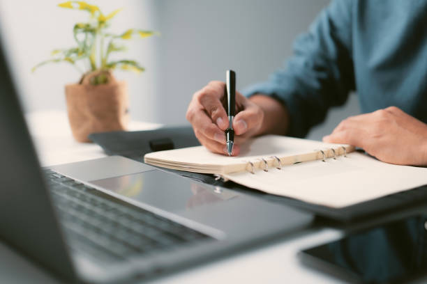 istock Male hands with pencil writing down list to do in notepad with laptop computer. Designer drawing sketch in notebook working on freelance 1339417622