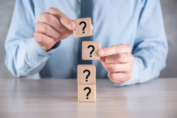 istock Businessman hold and put wooden cube block shape with question marks on grey table. Space for text.concept for confusion, question or solution 1339418233