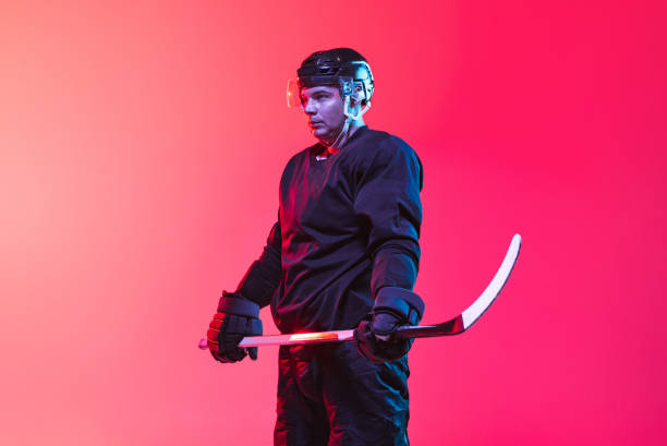 istock Cropped image of professional hockey playing in uniform with stick isolated over gradient pink background in neon 1339418510