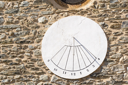 Closeup of an antique white stone sundial hanging on a stone wall