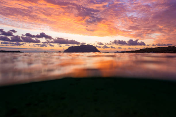 (Selective focus) Split shot, over under water surface. Defocused waves in the foreground with Tavolara Island on the surface during a dramatic sunrise. Porto Istana, Sardinia, Italy.
