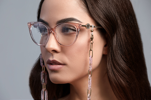 Portrait of a beautiful brunette woman in glasses close-up, attractive woman in stylish glasses on a gray background with healthy beautiful color skin, gray background, copy space.