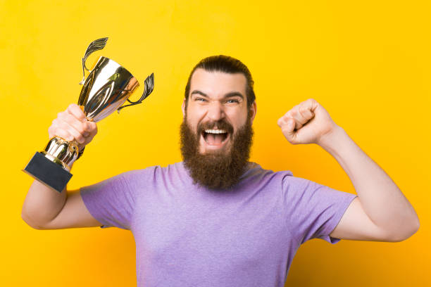 istock Screaming bearded man is making the winner gesture and holding a trophy. 1339425512
