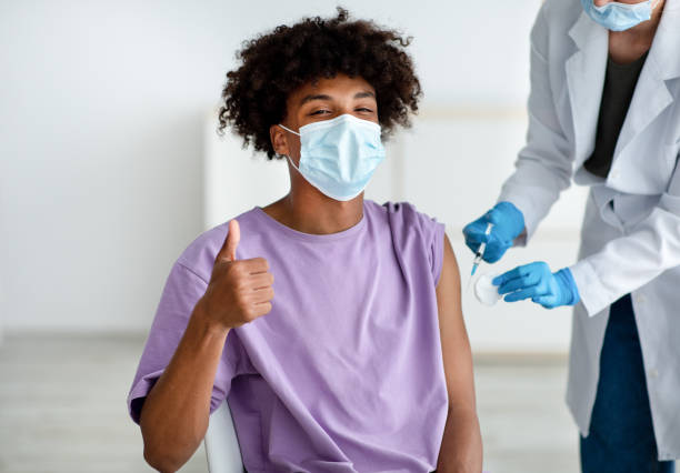 schwarzer teenager in gesichtsmaske macht daumen-hoch-geste während der covid-impfung, genehmigung der coronavirus-impfung - thumbs up african descent teenager women stock-fotos und bilder