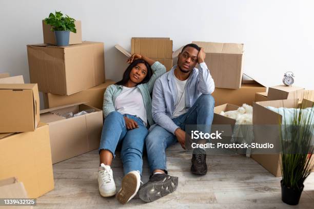 Sad Black Spouses Exhausted After Moving To New Apartment Sitting Among Cardboard Boxes And Resting Stock Photo - Download Image Now