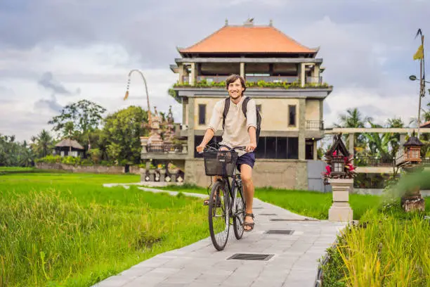 Photo of A young man rides a bicycle on a rice field in Ubud, Bali. Bali Travel Concept