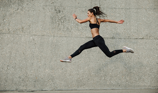 Female athlete running and jumping. Side view of flexible female athlete exercising outdoors.