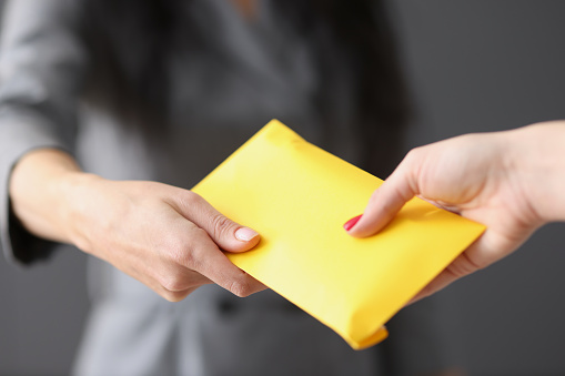 Woman hands yellow closed envelope with money to employee. Fraud and premiums in envelopes concept