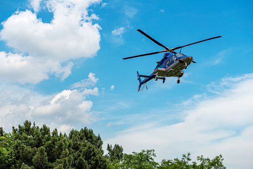 Helicopter landing above the trees in front of the cloud landscape.