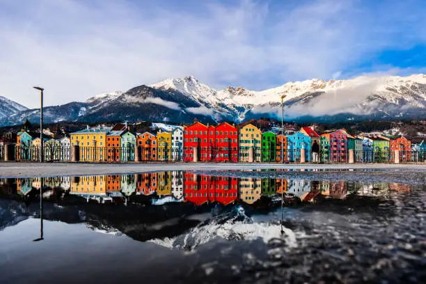 Water reflection of the colourful cityscape of Innsbruck at the Mariahilf district with the snowy Nordkette mountain chain.