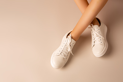 White sneakers shoes and girlâ€™s legs on nude background - casual footwear