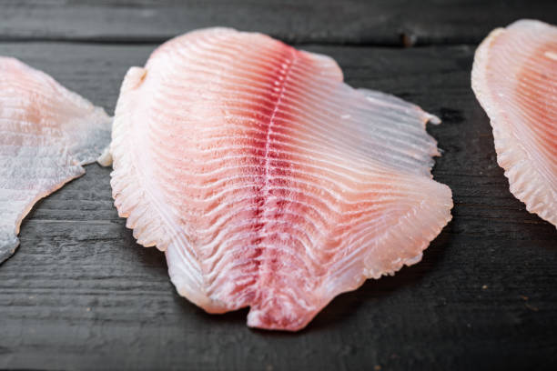 istock Tilapia fish skinless meat, on black wooden table 1339441010
