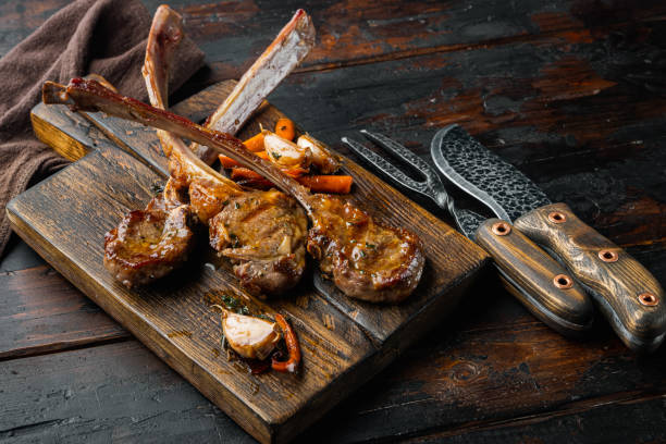 istock Barbecue dinner. Grilled lamb meat chops with onion and thyme, on wooden serving board, on old dark  wooden table background 1339443224