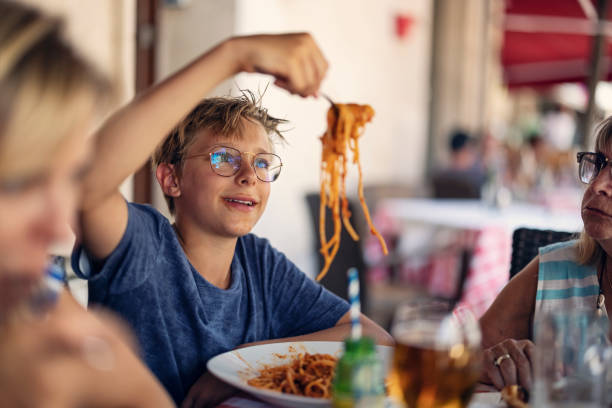 Family having lunch in the street restaurant Family enjoying a lunch in the street restaurant. Teenage boy is eating a spaghetti.
Sunny summer day.
Canon R5 kids eating noodles stock pictures, royalty-free photos & images