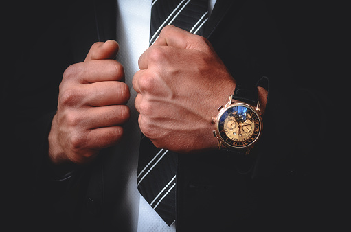 A stylish men's watch on the hands of a guy in a suit on a black background.