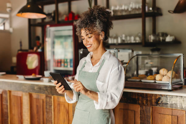 glückliche cafébesitzerin, die ihr geschäft auf einem digitalen tablet führt - kleinunternehmen stock-fotos und bilder