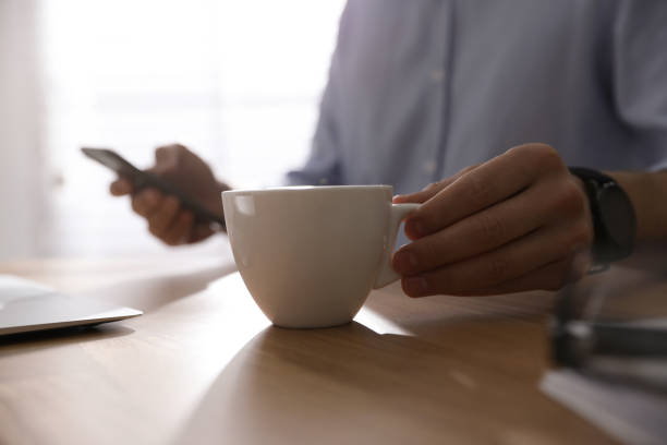 istock Man with cup of coffee at table indoors, closeup 1339445674