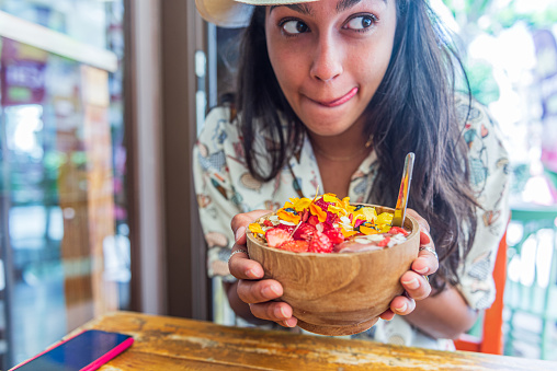 Close up woman with wooden bowl of fruit salad with edible flowers
