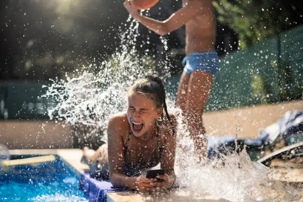 Photo of Teenage boy splashing his sister with bucket of water