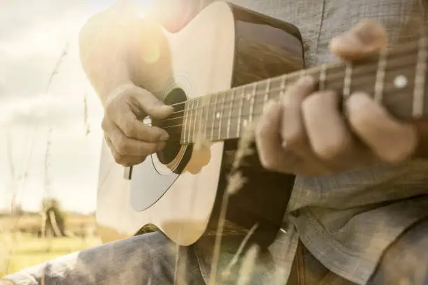 Photo of Guitarist playing acoustic guitar outside in field