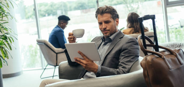 Businessman Using Digital Tablet and Drinking Coffee while Waiting for his Flight in the Airport VIP Lounge