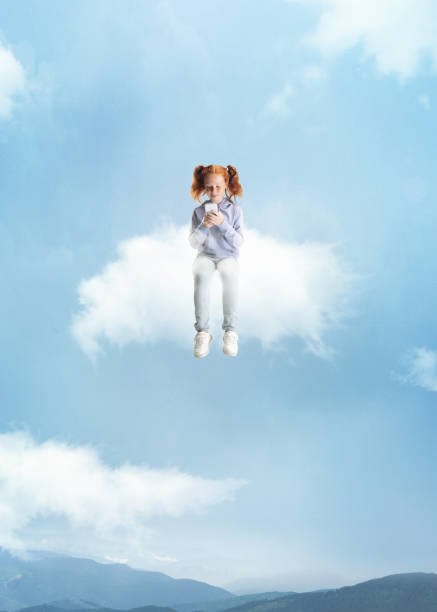 istock Conceptual collage with little beautiful girl sitting on white cloud using phone and flying at sky, outdoors. Concept of childhood, happiness, dreams, adventure 1339457157