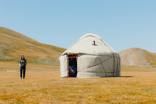 Woman explorer with long hair walking at the meadow near the traditional yurt enjoying the sunny summer morning at Tian Shan mountains, Central Asia