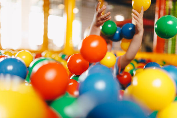 Happy child playing at balls pool playground. Kid playing with multi coloured plastic balls in big dry paddling pool in playing centre. School boy having fun in indoor park playground