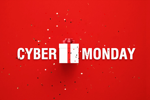 Cyber Monday text and black gift box sitting behind gold colored confetti over red background. Horizontal composition with copy space. Directly above. Great use for Cyber Monday concepts.