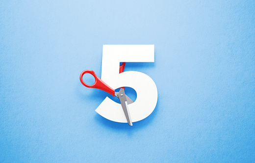 Red scissors cutting the number five over blue background. Horizontal composition with copy space.