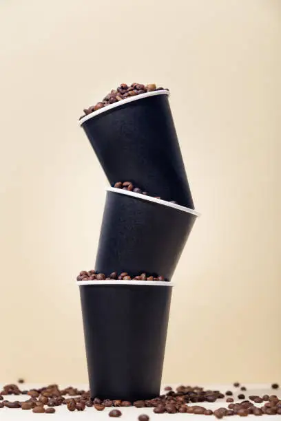 Paper coffee cups filled with coffee beans, on a beige background