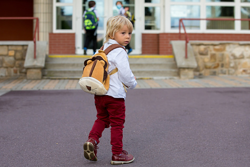 Preschool blond child, cute boy in uniform, hodling apple and book, going in preschool for the first time after summer vacation