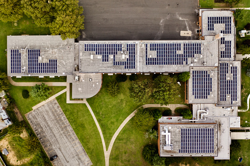 A top down shot directly above a building with solar panels on the roof, taken during the day. . The surrounding landscape well kept, it is an environmentally friendly establishment.