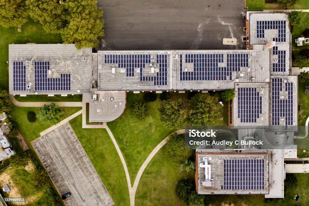 Top down shot directly over a School with Solar Panels on the roof. A top down shot directly above a building with solar panels on the roof, taken during the day. . The surrounding landscape well kept, it is an environmentally friendly establishment. School Building Stock Photo