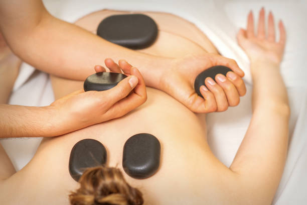 スパサロンで黒いマッサージ石を持つマッサージ師の手で女性の背中にホットストーンマッサージ。 - massaging spa treatment stone massage therapist ストックフォトと画像