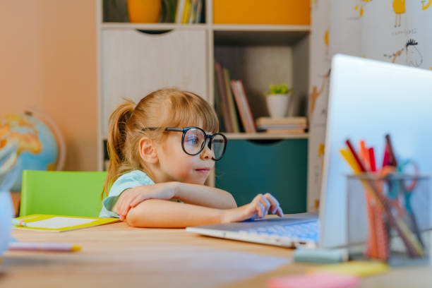istock Little girl elementary student studying online from home using laptop sitting at the desk 1339476865