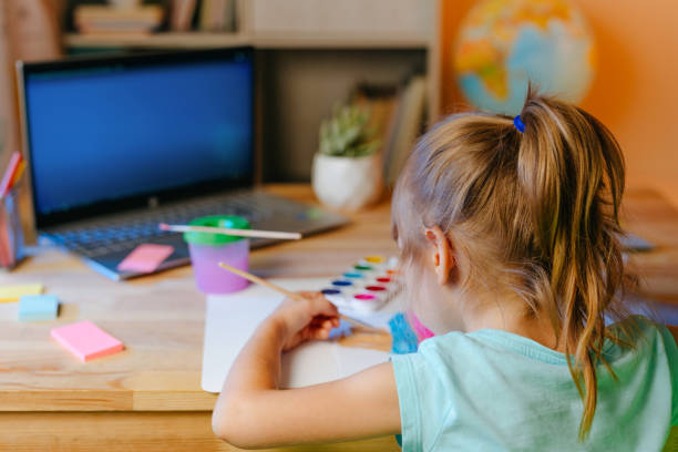 istock Little girl elementary student drawing studying online from home using laptop sitting at the desk 1339476925