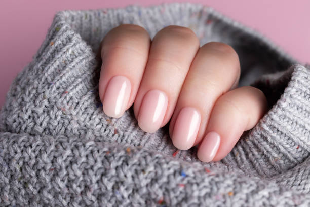 Hand in sweater with nude nails on pink background